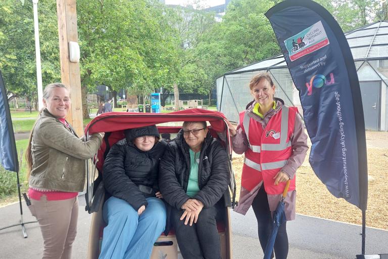 Participants and volunteers with a Cycling Without Age trishaw at a Portsmouth carers' event.