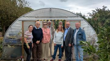 A group of people stand outside a poly tunnel on an allotment