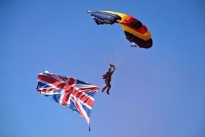 A military parachutist in the sky with a parachute above and Union Flag below them