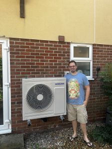 Man in blue shirt standing next to grey air source heat pump