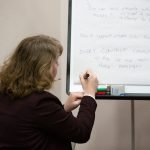 A female speaker writing on a white board at the social value workshop in 2023