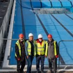 four people in hard hard hats and high vis jackets stood by a newly refurbished empty pool