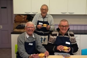 Three men wearing navy aprons hold their homemade pies and smile.
