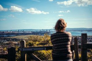 Young woman looks down over scenery including the sea, from the top of Portsdown Hill
